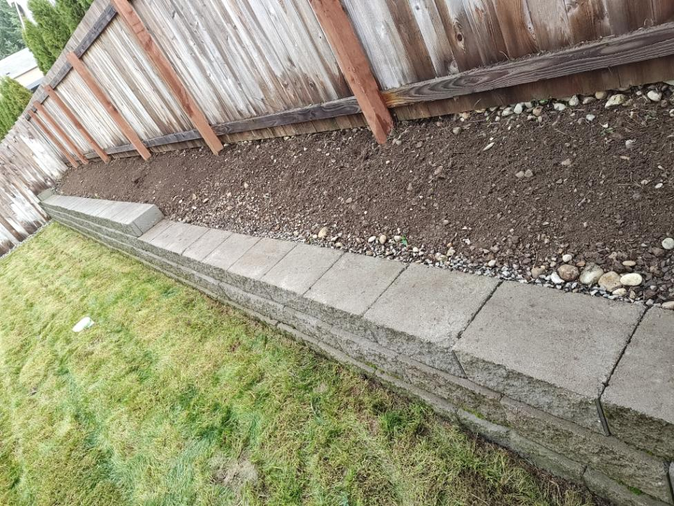 Concrete paver border and edging along wooden fence with gravel fill, showing professional hardscaping work.