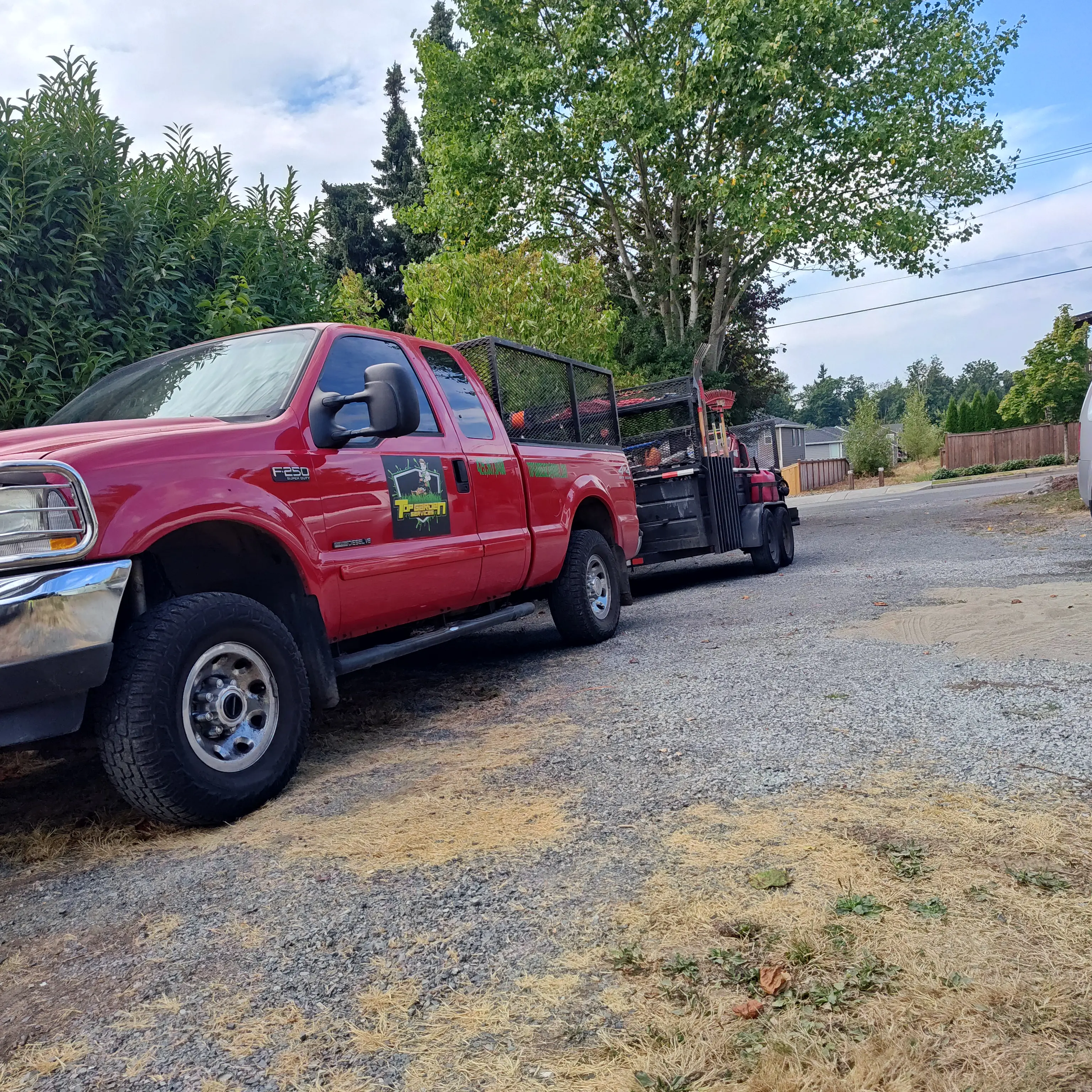 Red Ford F-250 work truck with professional landscaping trailer parked on residential street, ready for service.